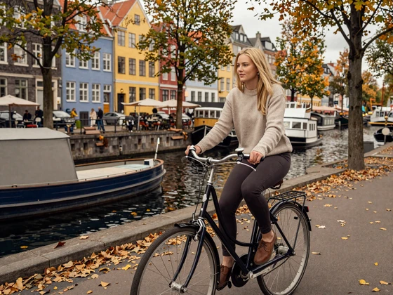 Danish woman cycling along a Copenhagen canal with autumn foliage - Danish dating lifestyle